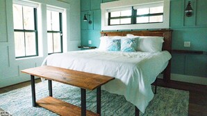 A bedroom with a bed, a wooden bench, and two windows. - Charming 1-bedroom house with WiFi and AC in Cowpens (Cowpens)