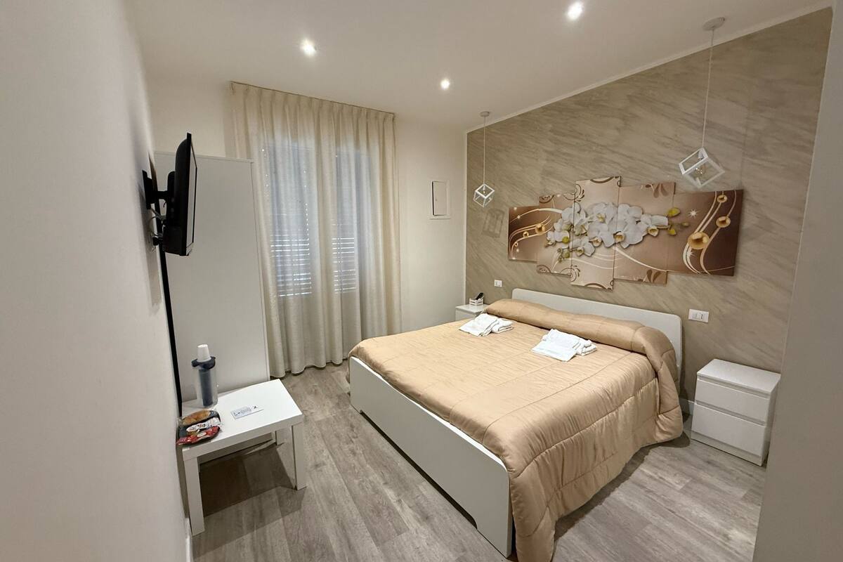 A modern bedroom with a bed, bedside tables, a desk, and a wall-mounted TV.