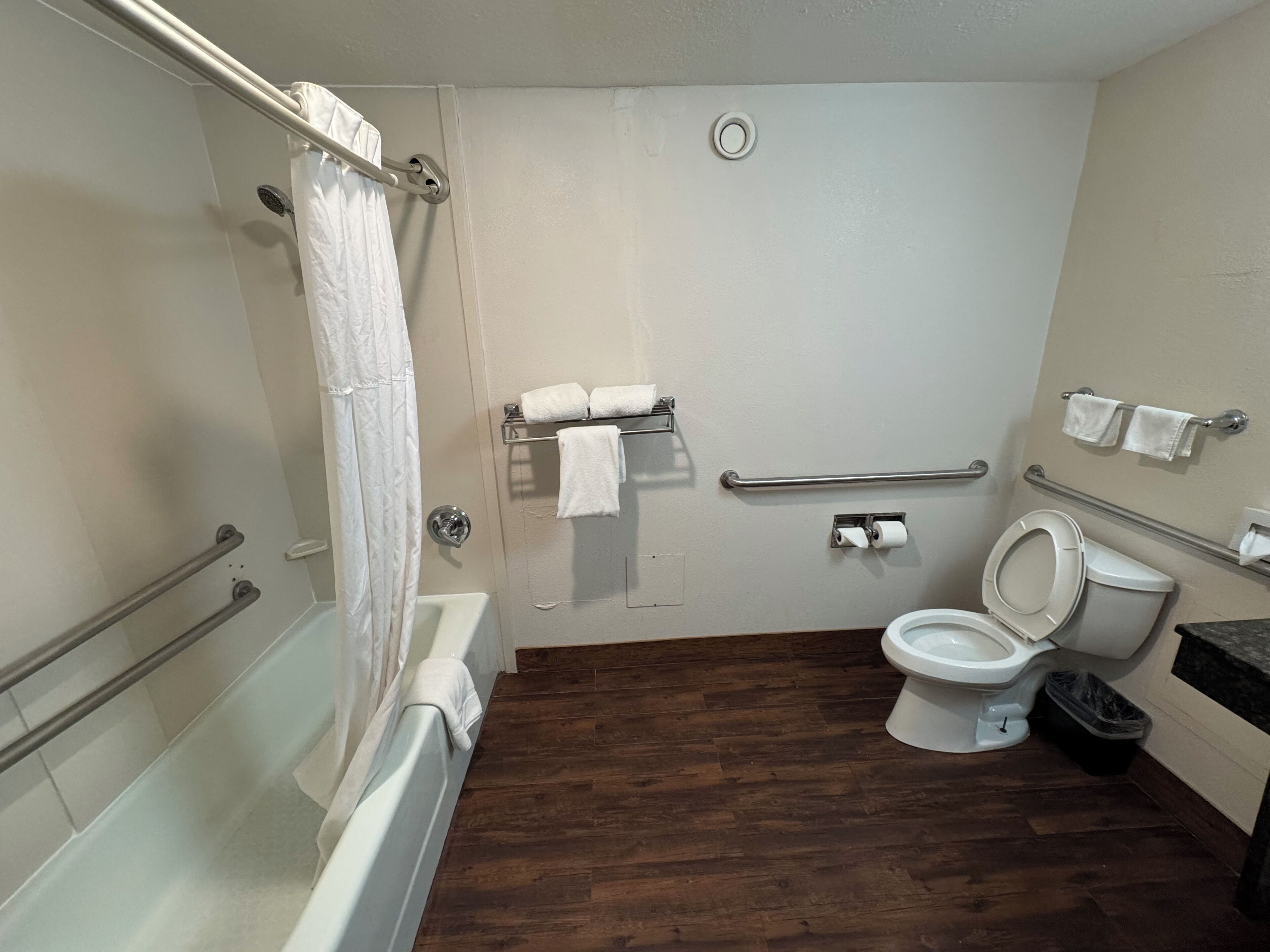 A bathroom with a bathtub, toilet, and shower. It includes grab bars and a handrail.