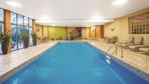 Une piscine intérieure à l’eau d’un bleu cristallin, entourée de chaises longues et de plantes en pot.