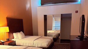 Une chambre d’hôtel avec deux lits, un bureau avec une lampe, une télévision et une moquette à motifs.