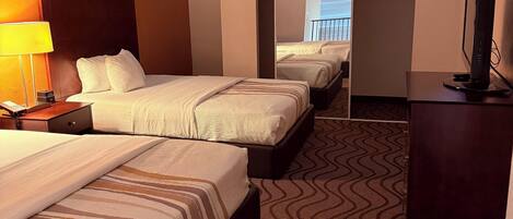A hotel room with two beds, a desk with a lamp, a television, and a patterned carpet.