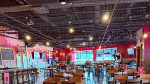 Un restaurant spacieux avec de hauts plafonds, des poutres apparentes et des guirlandes lumineuses. Les tables et les chaises sont disposées dans un espace ouvert.