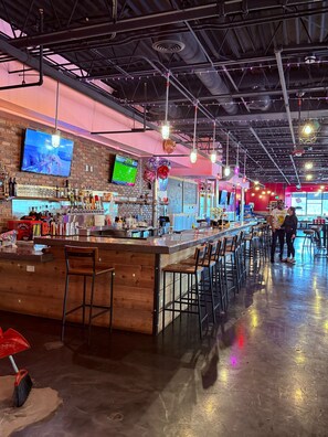 A bar area with a long counter, multiple stools, and a TV screen displaying a sports game. - Mountain Valley Inn & Suites (Silverthorne)