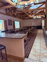 A spacious dining area with high ceilings and exposed wooden beams, featuring a central island with a granite countertop and bar stools.