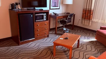 Habitación de hotel con televisión, escritorio con silla, refrigerador pequeño, microondas, sofá y alfombra estampada.