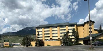 A multi-story hotel with a flat roof, located in a mountainous area with a parking lot in front.