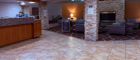 A lobby with a reception desk, seating area, stone pillars, and a flat-screen TV.