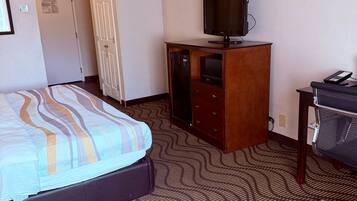 Una habitación de hotel con una cama, un televisor sobre un mueble de madera, un escritorio con una silla y una alfombra estampada.