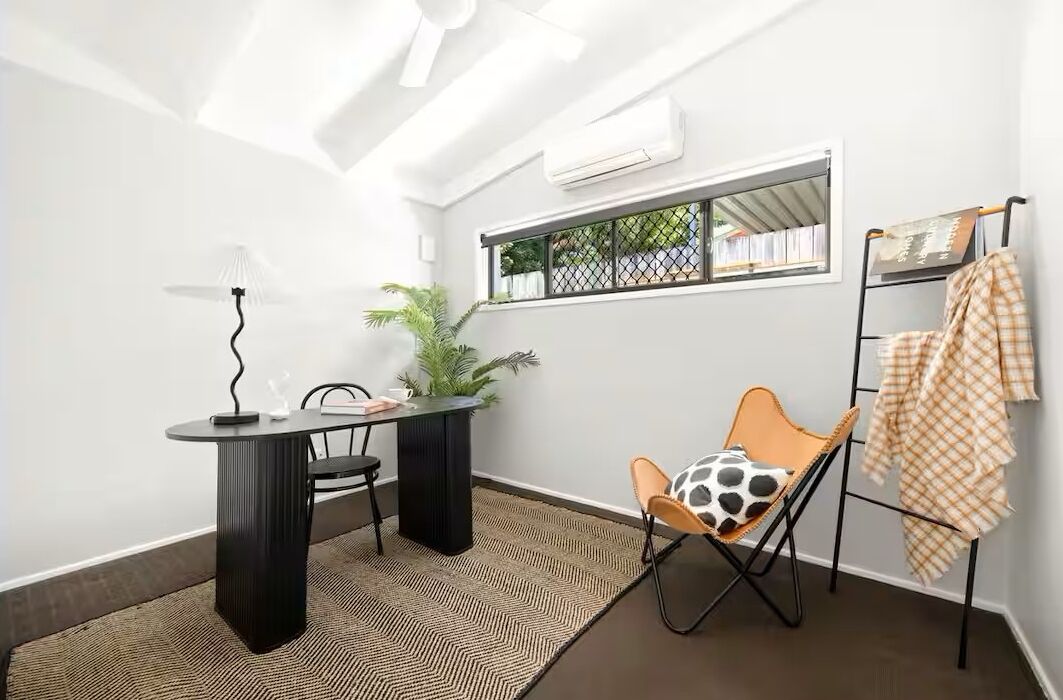 Ein kleines Zimmer mit rundem Tisch, einem Sessel, einer Stehlampe, einem Blumentopf und einem Fenster mit Blick.