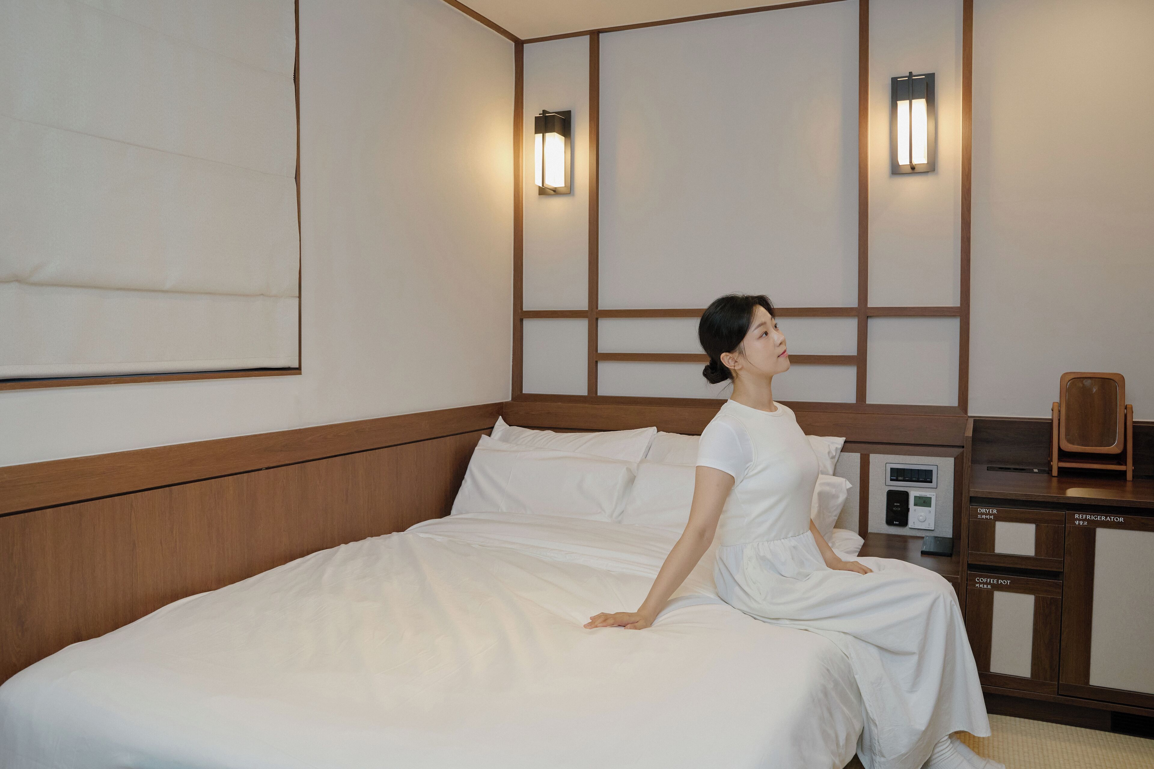 Una habitación de hotel con una cama, una mesita de noche con cafetera y dos lámparas fijadas a la pared.