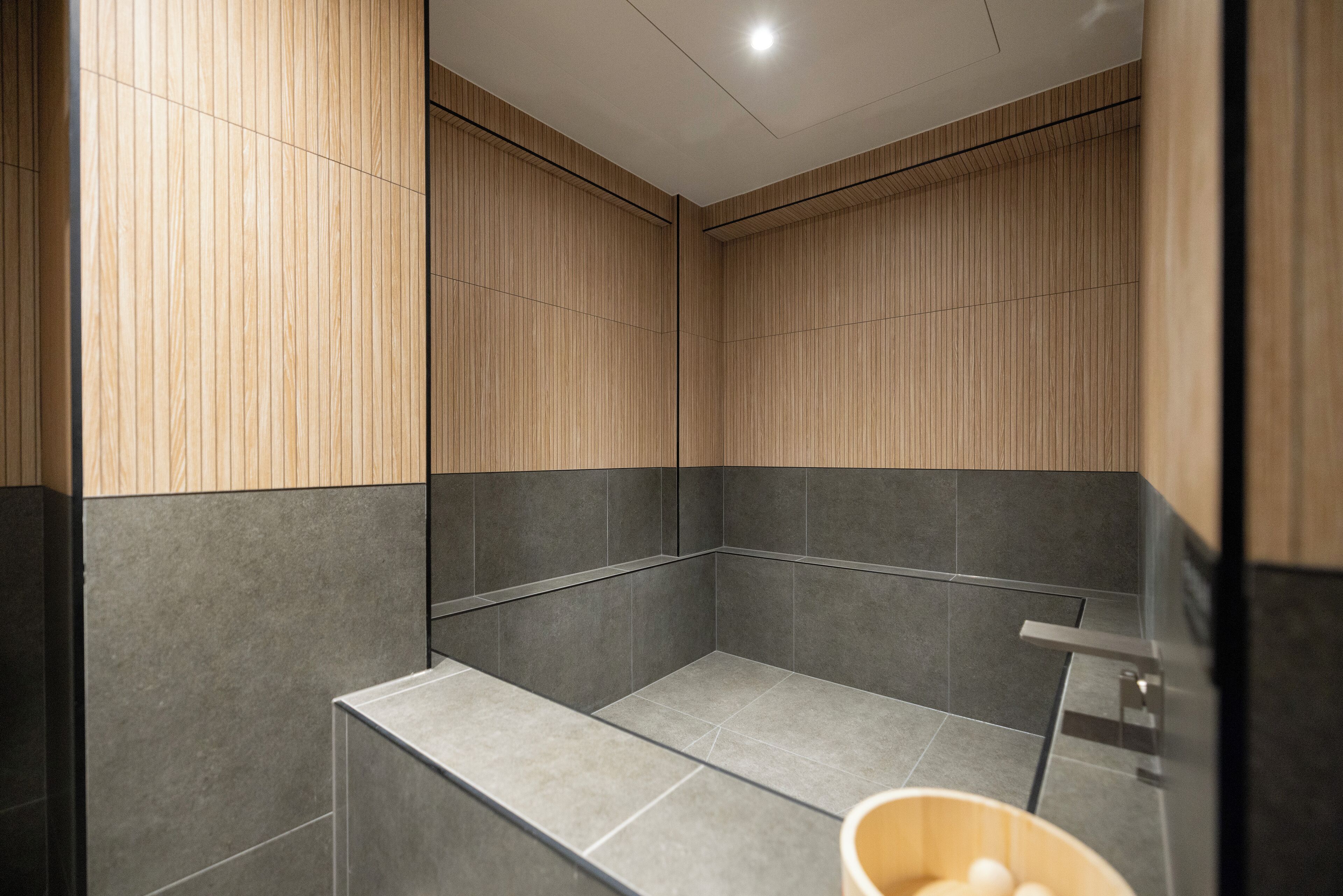 A modern bathroom with wooden paneling and grey tiles.