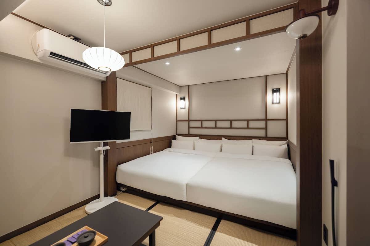 A hotel room with a large bed, a flat-screen TV, an air conditioning unit, and a bedside table.
