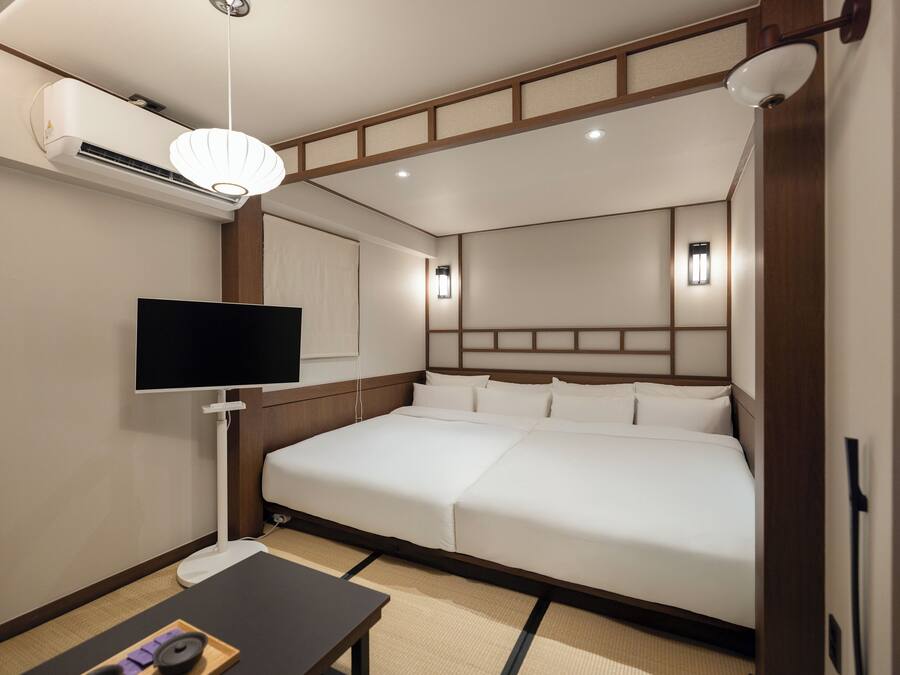 Una habitación de hotel con una cama grande, un televisor de pantalla plana, un equipo de aire acondicionado y una mesita de noche.