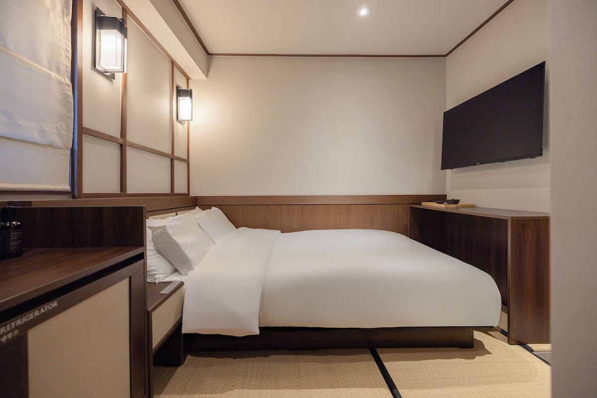 A hotel room with a bed, bedside tables, a flat-screen TV, and wall-mounted lights.