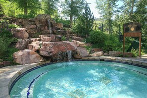 A swimming pool with a waterfall feature, surrounded by rocks and greenery.