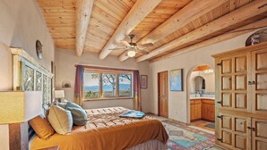 Une chambre avec un plafond en bois, un lit recouvert d’une couverture marron, une table de chevet, une fenêtre donnant sur un beau paysage et une armoire.