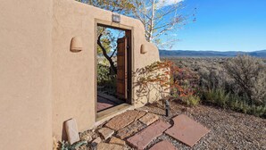 Un bâtiment rustique en adobe, doté d’une porte en bois, d’escaliers en pierre et offrant une vue sur le paysage environnant.