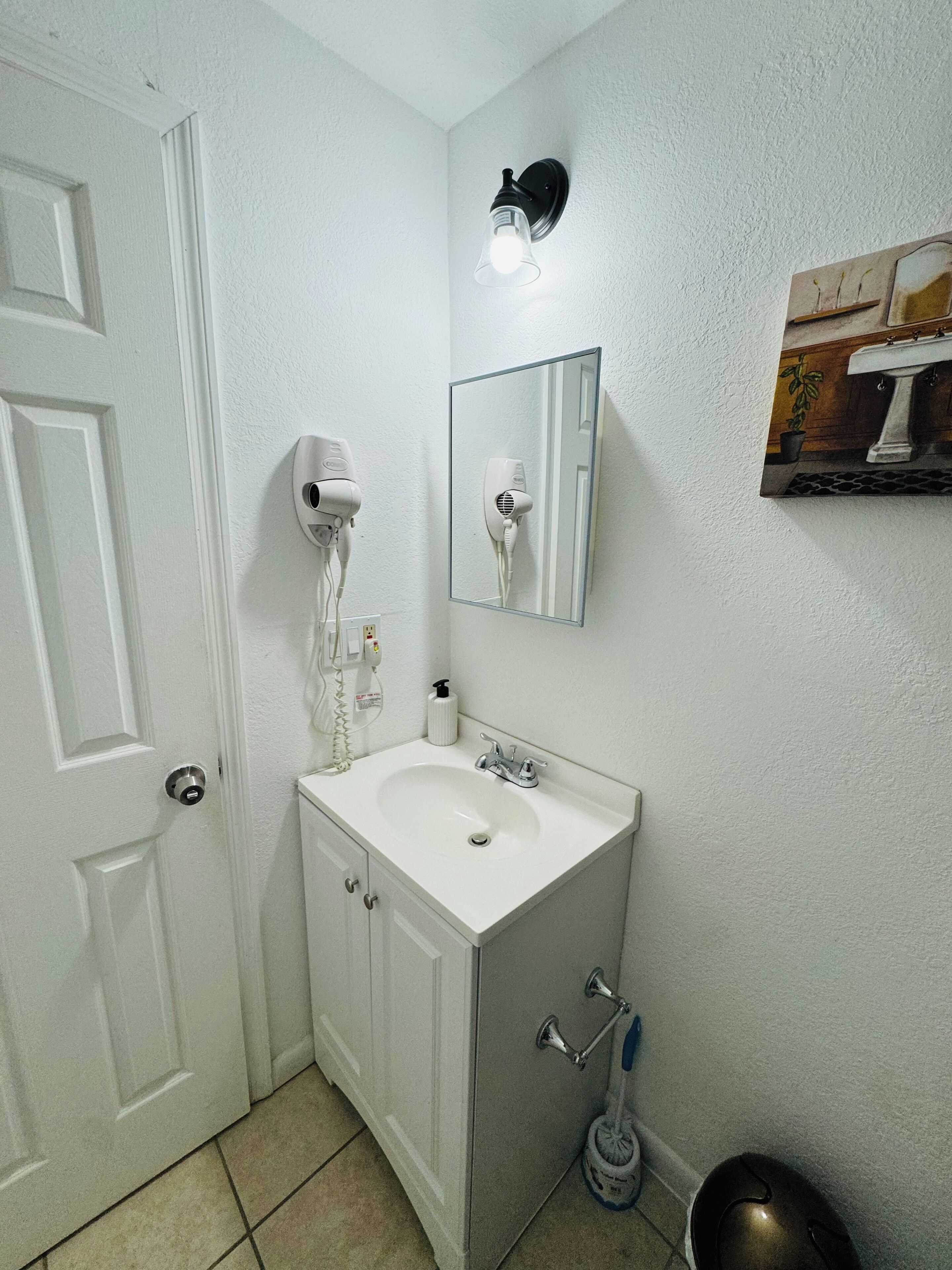 A bathroom with a white sink, a mirror, a hairdryer, and a towel dispenser.