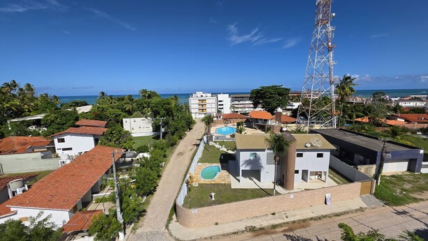 A coastal residential area with a prominent communication tower, a swimming pool, and a mix of single and multi-story buildings. - Nawa Beach Residence 301 by La Playa  (Tamandaré)