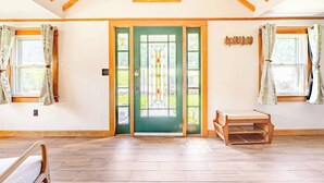 A spacious room with a high ceiling, wooden beams, a green door with stained glass, and a bench.