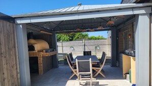 Een terras buiten met een tafel, stoelen, een grill en een barbecuehoek.