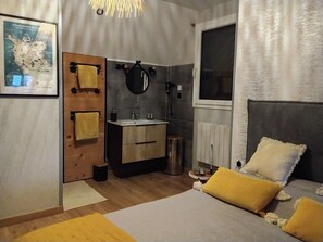 Un dormitorio moderno con puerta de madera, un espejo redondo, un lavabo y una cama con almohadas amarillas.