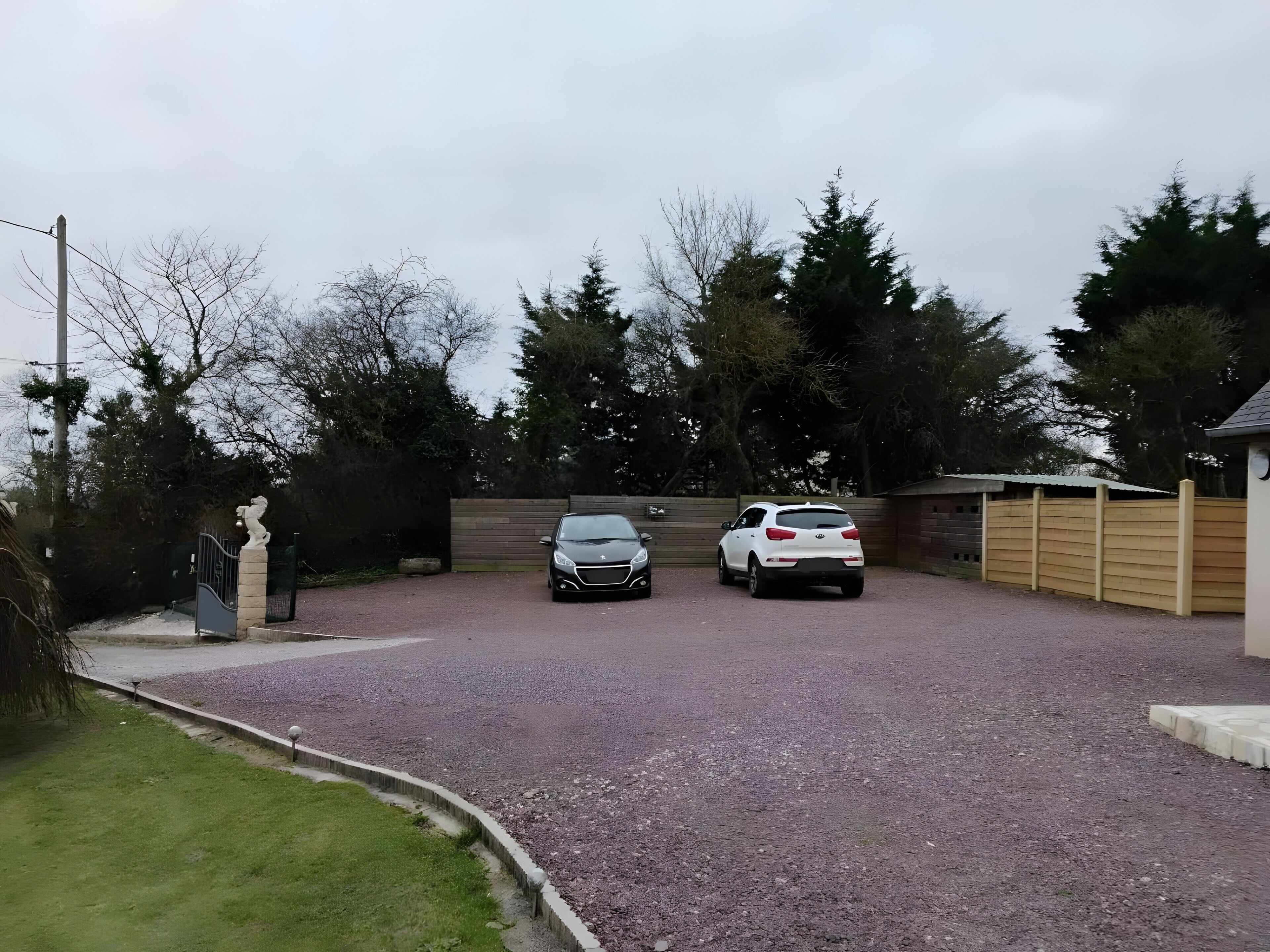 A gravel driveway with two cars parked, a statue, and a wooden fence.