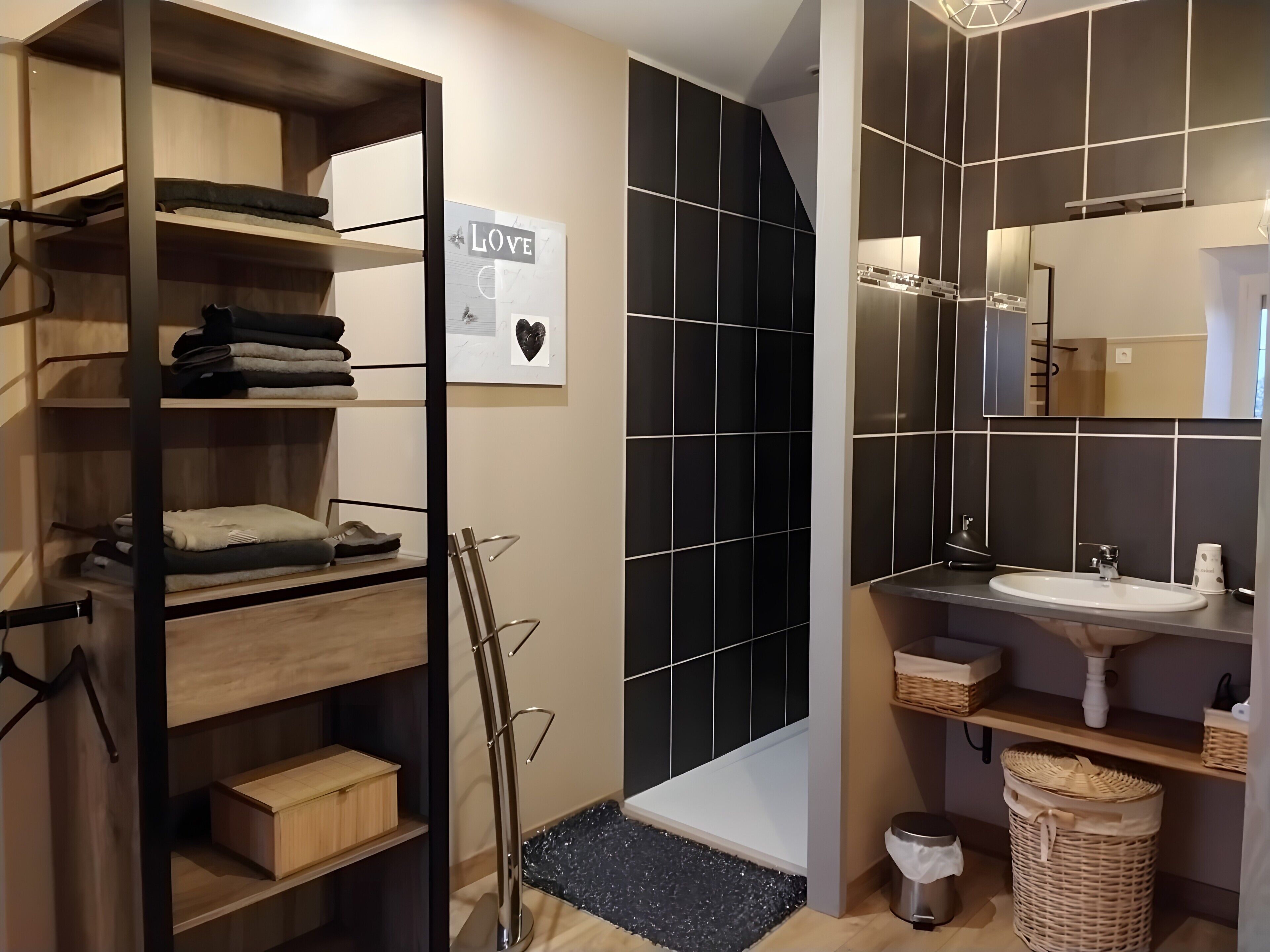 A modern bathroom with a sink, mirror, and black tiled walls.