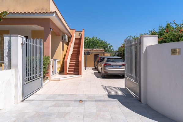 A residential area with a gated entrance, a staircase leading to a covered porch, and parked cars.