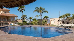A swimming pool with a lifeguard chair, lounge chairs, palm trees, and a building with a tiled roof.