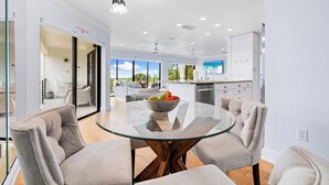 A modern kitchen with white cabinets, a dining area with a glass table, and a view of the outdoors. - Breathtaking Beach Views - 3bed on Siesta! (Siesta Key)