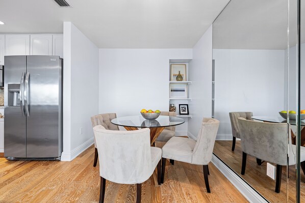 A modern kitchen with a stainless steel refrigerator, a round glass table with chairs, and a wooden floor. - Breathtaking Beach Views - 3bed on Siesta! (Siesta Key)