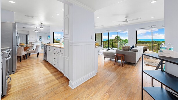 A modern kitchen with white cabinetry, a dining area with a wooden table and chairs, and a living area with a sofa and a view of the ocean. - Breathtaking Beach Views - 3bed on Siesta! (Siesta Key)