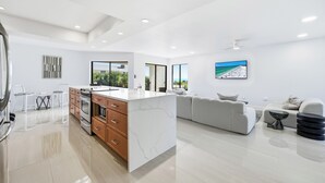 A modern kitchen with a marble island, wooden cabinets, and a dining area with clear chairs. - 3bed on Siesta w/ direct beach access! (Siesta Key)