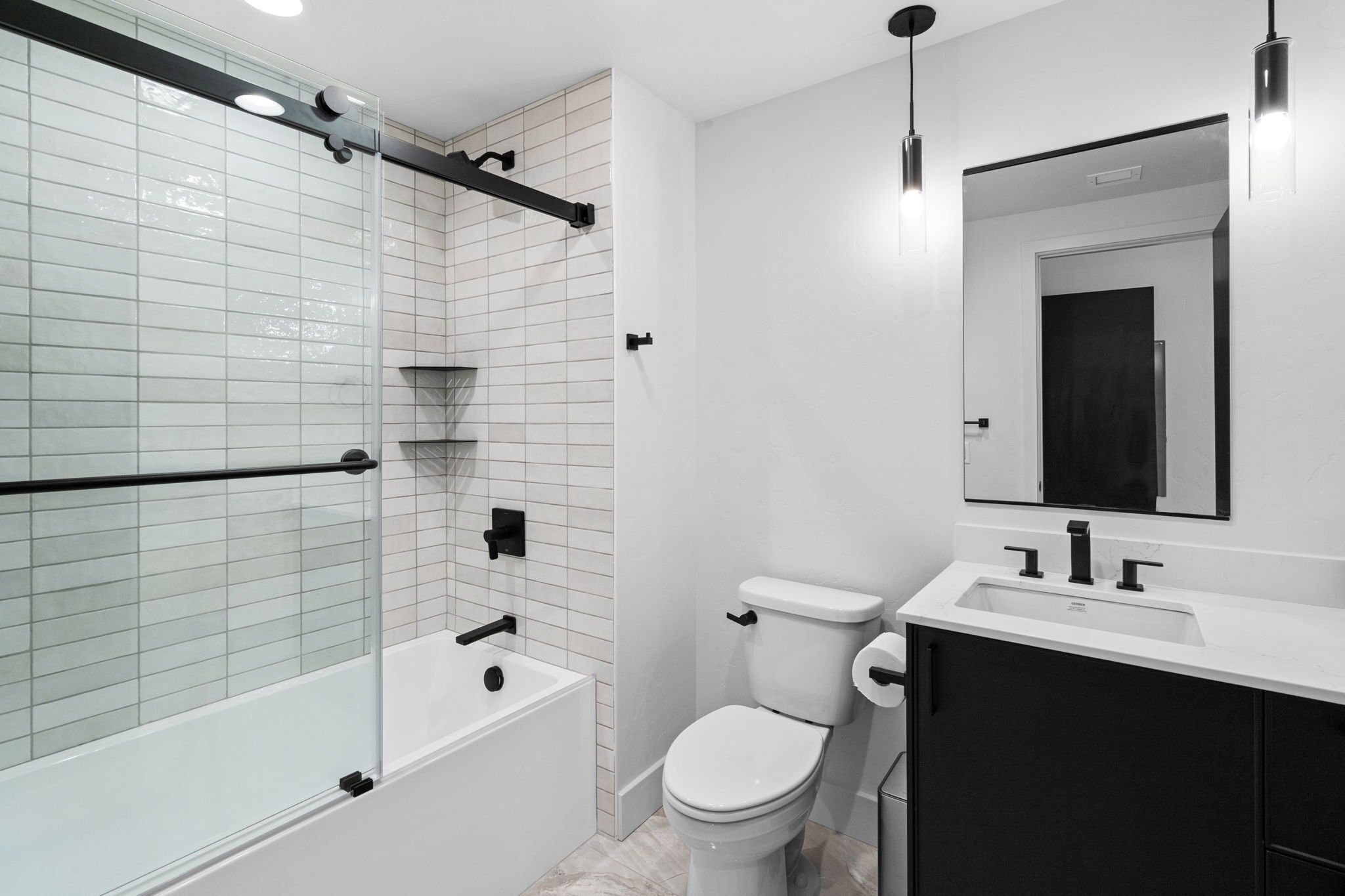 A modern bathroom with a glass shower enclosure, a white toilet, and a black vanity with a mirror.