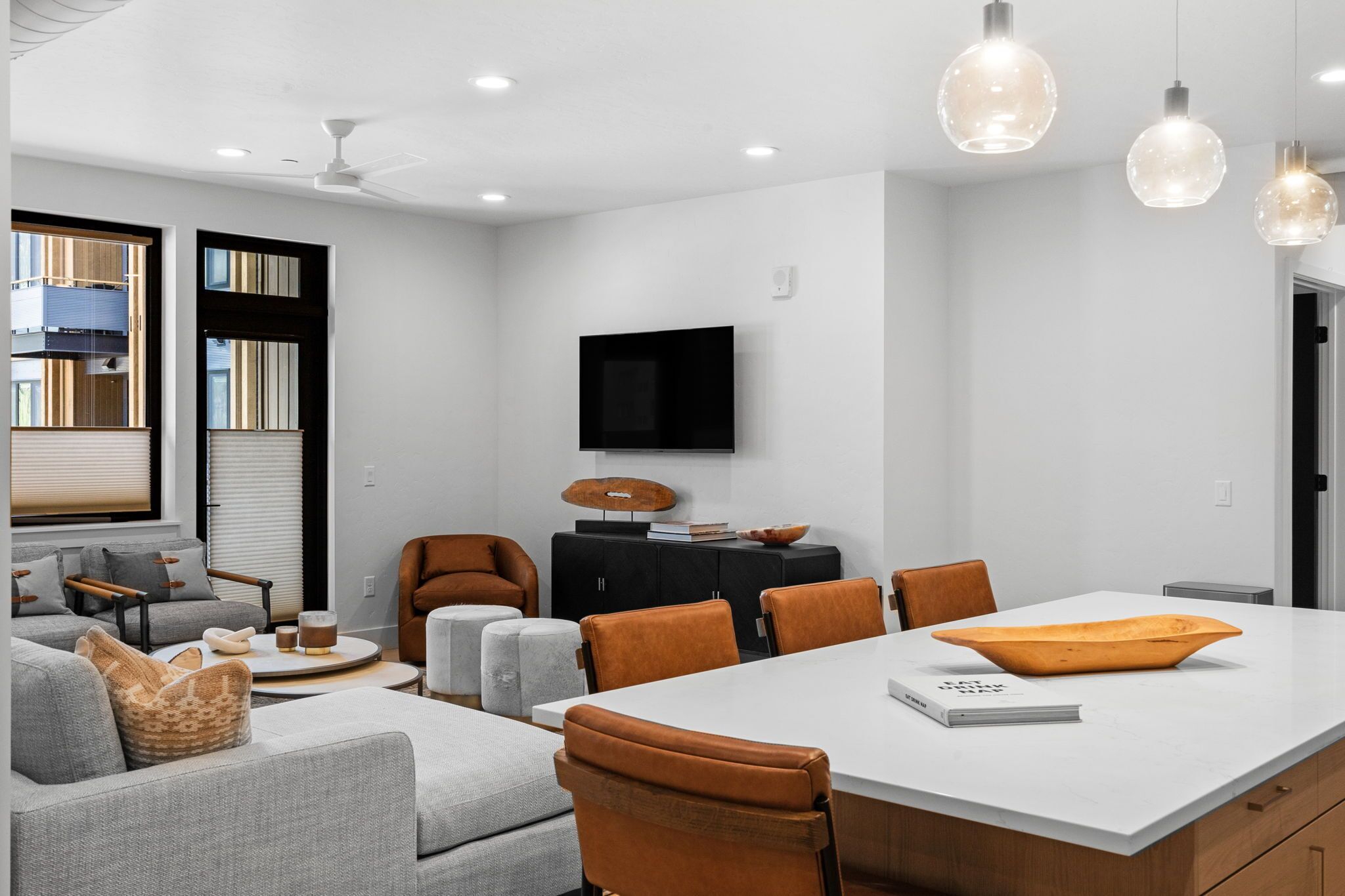A modern living room with a large white island table, grey sofas, and orange chairs.