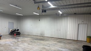 A spacious indoor area with a concrete floor, a lawnmower, and a trash bin.