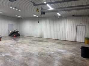Een ruime binnenruimte met een betonnen vloer, een grasmaaier en een vuilnisbak.