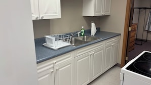 A kitchen with white cabinets, a granite countertop, a stainless steel sink, and a dish rack.