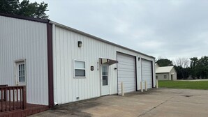 A white industrial building with a metal exterior, a wooden deck, and a large garage door.