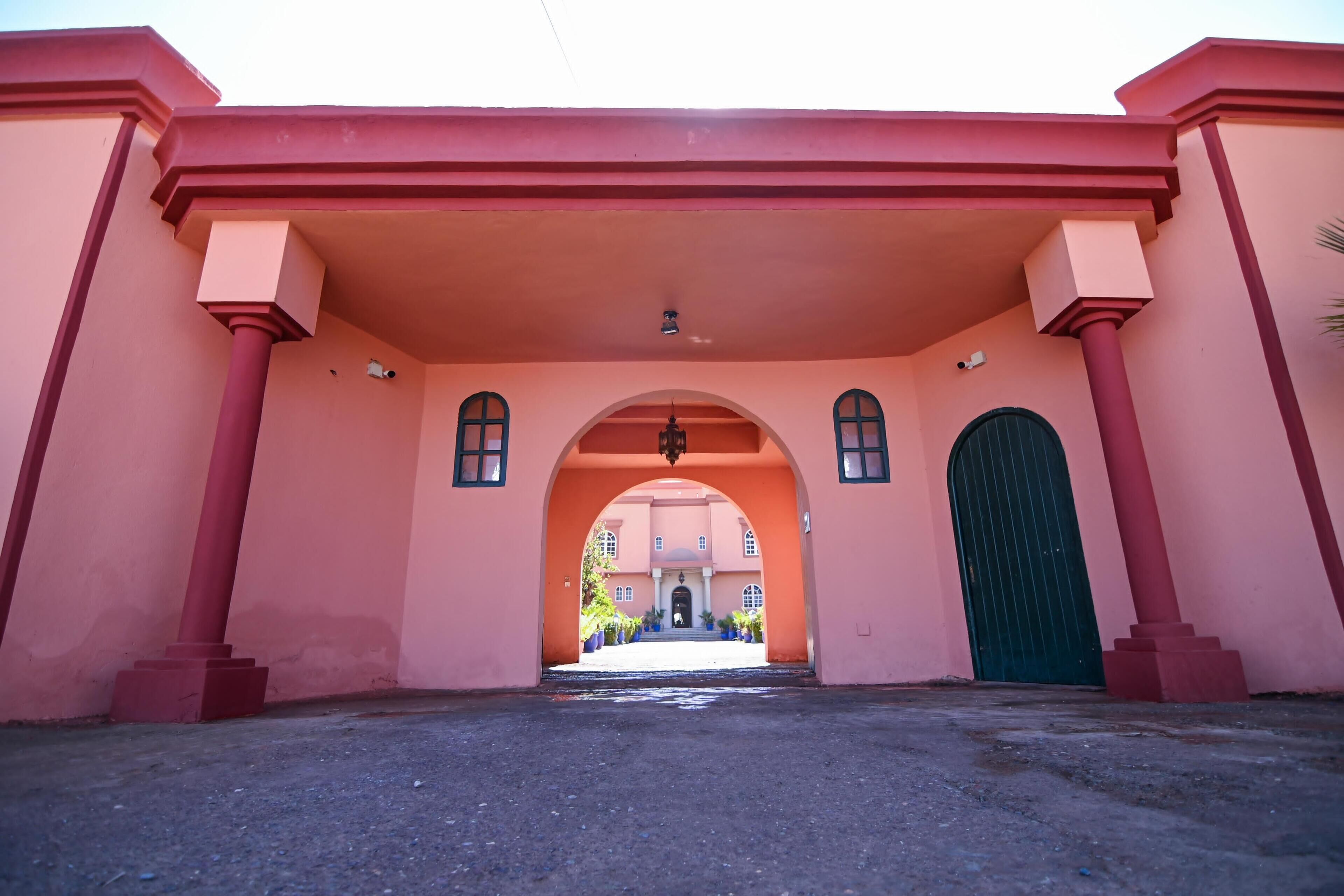 A building entrance with a red archway, a green door, and a view of a building in the background.