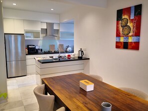 Eine moderne Küche mit Edelstahlgeräten, einem Holztisch und einem farbenfrohen, abstrakten Gemälde an der Wand.