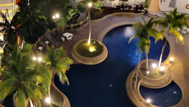 Vue aérienne d’un espace piscine d’hôtel, avec plusieurs éléments aquatiques de forme circulaire et des palmiers.