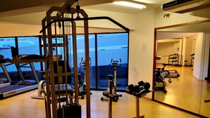Une salle de sport équipée de divers appareils d’exercice, dotée de grandes fenêtres et d’un plancher en bois.