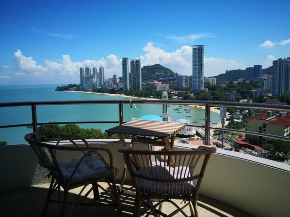 Ein Balkon mit Korbstühlen und einem Tisch mit Blick auf Strand und Stadtlandschaft.