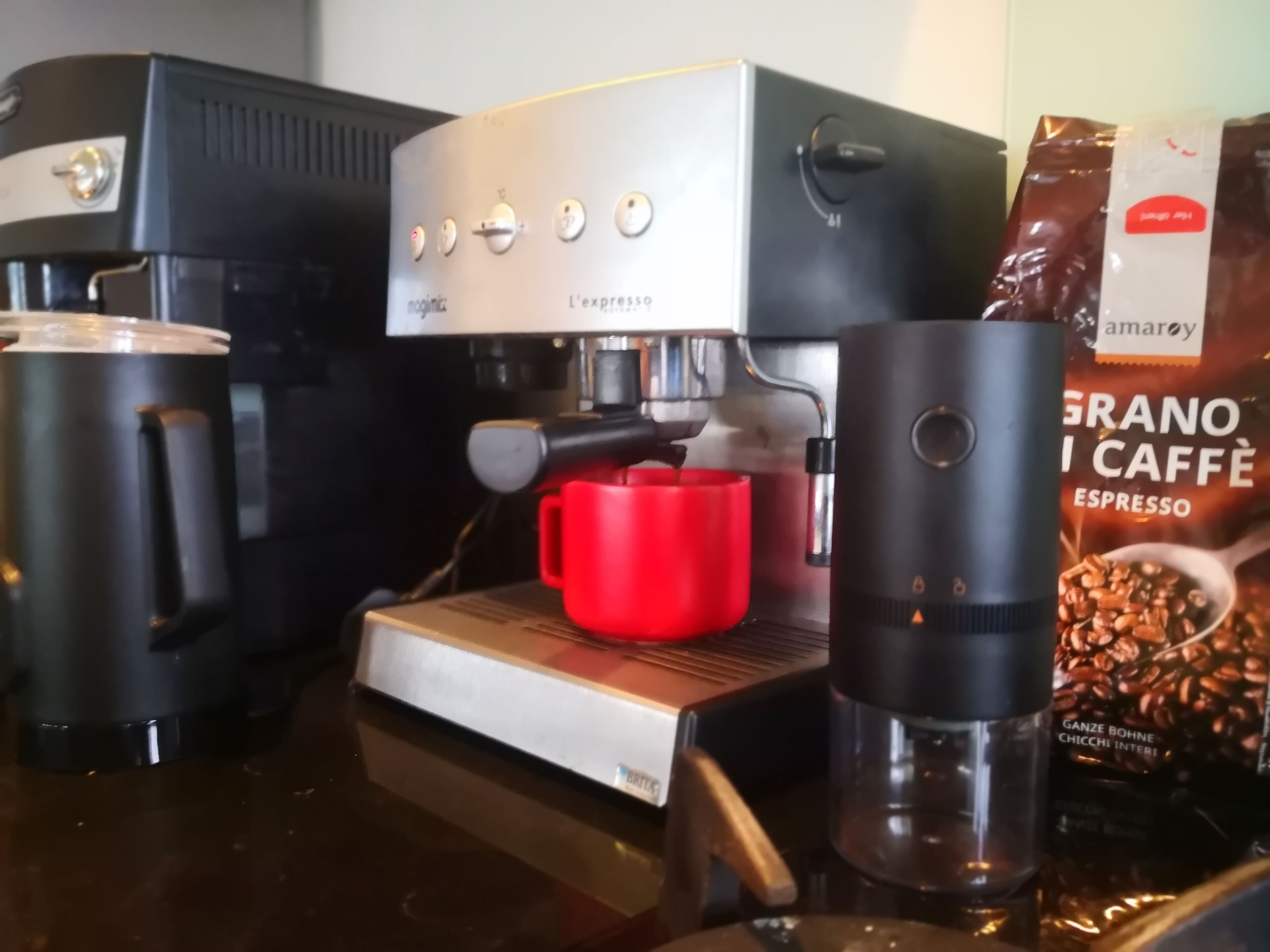 A coffee machine with a red mug, a grinder, and a bag of coffee beans.