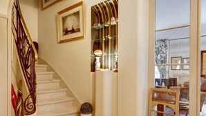 A staircase with a wooden handrail, a potted plant, and a chair in a well-lit room with a large window and a framed picture on the wall.