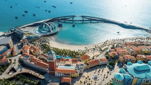 Vista aérea de un pueblo costero con un puente destacado, una plaza central y edificios circundantes con estilos arquitectónicos diversos.