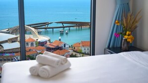 Habitación de hotel con cama, ventana con vista al mar, un puente y un paisaje urbano.